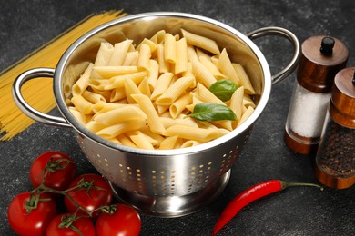 Photo of Cooked pasta in metal colander, products and spices on dark textured table, closeup