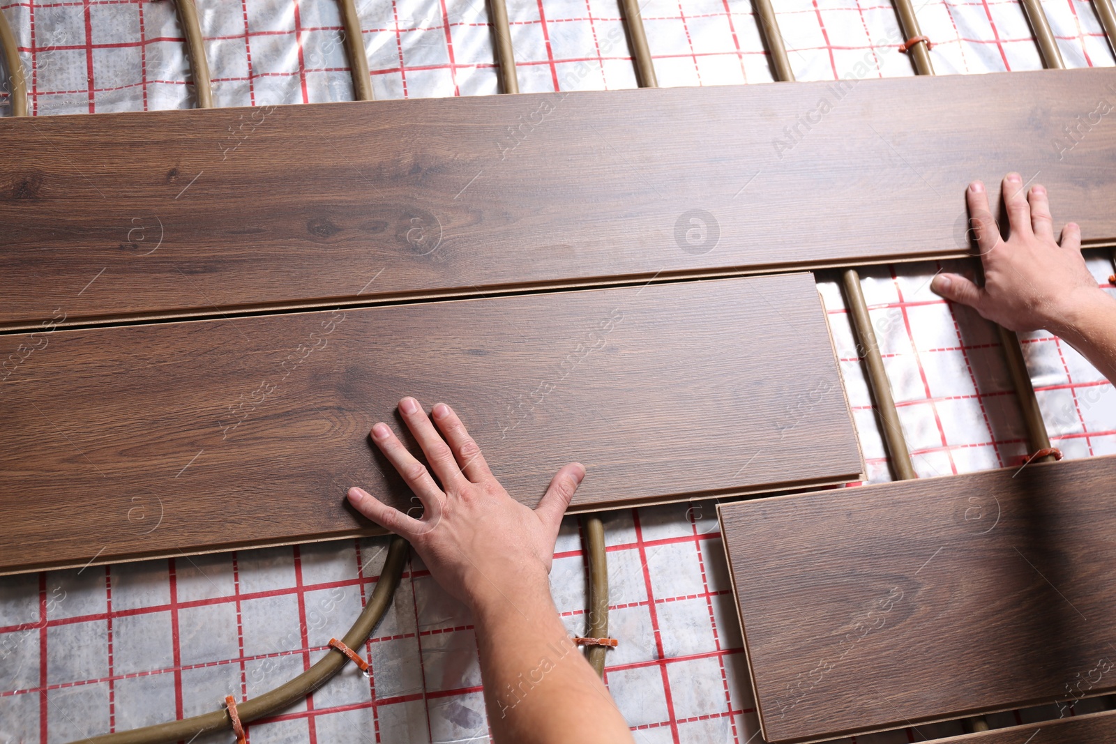 Photo of Worker installing new wooden laminate over underfloor heating system, closeup