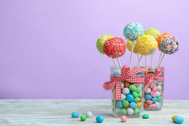 Photo of Glass jars with tasty cake pops and dragee on table against lilac background, space for text