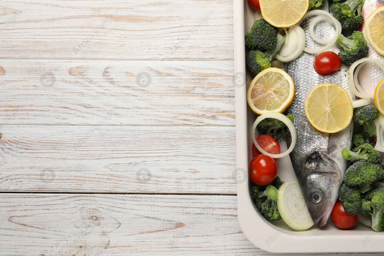 Photo of Raw fish with vegetables and lemon in baking dish on wooden table, top view. Space for text