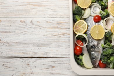 Photo of Raw fish with vegetables and lemon in baking dish on wooden table, top view. Space for text