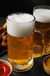 Photo of Mugs with delicious beer on dark grey table, closeup