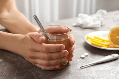 Photo of Woman holding glass with hot tea for cold on table