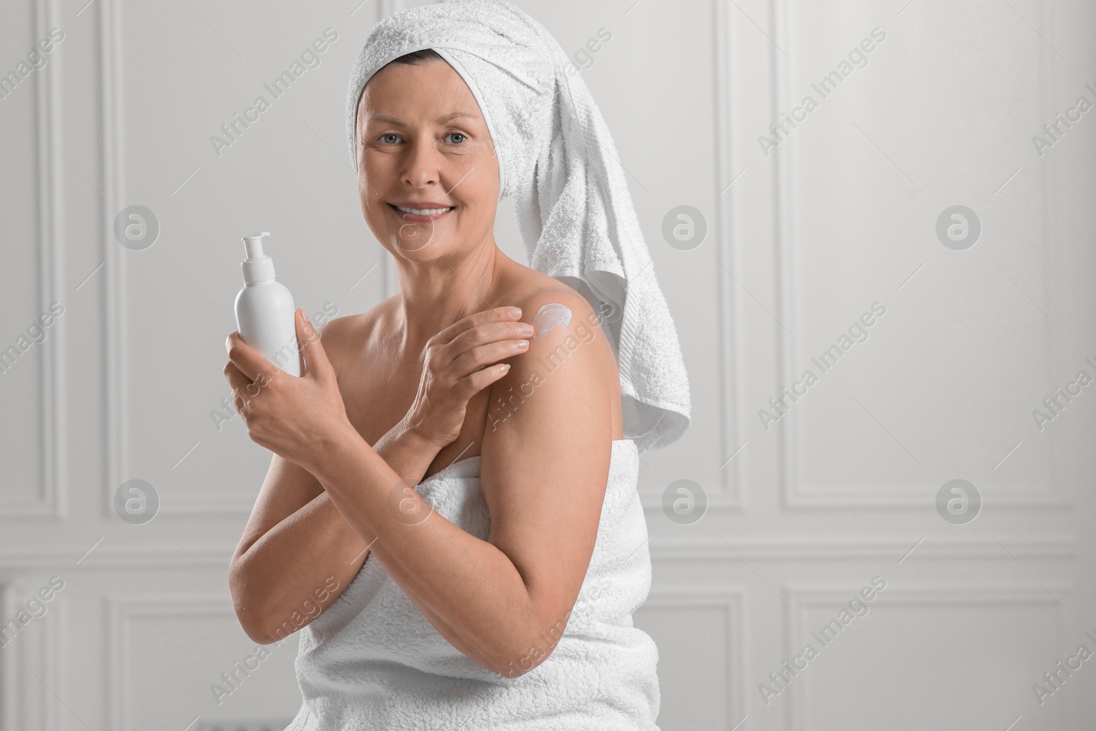 Photo of Happy woman applying body cream onto shoulder near white wall. Space for text