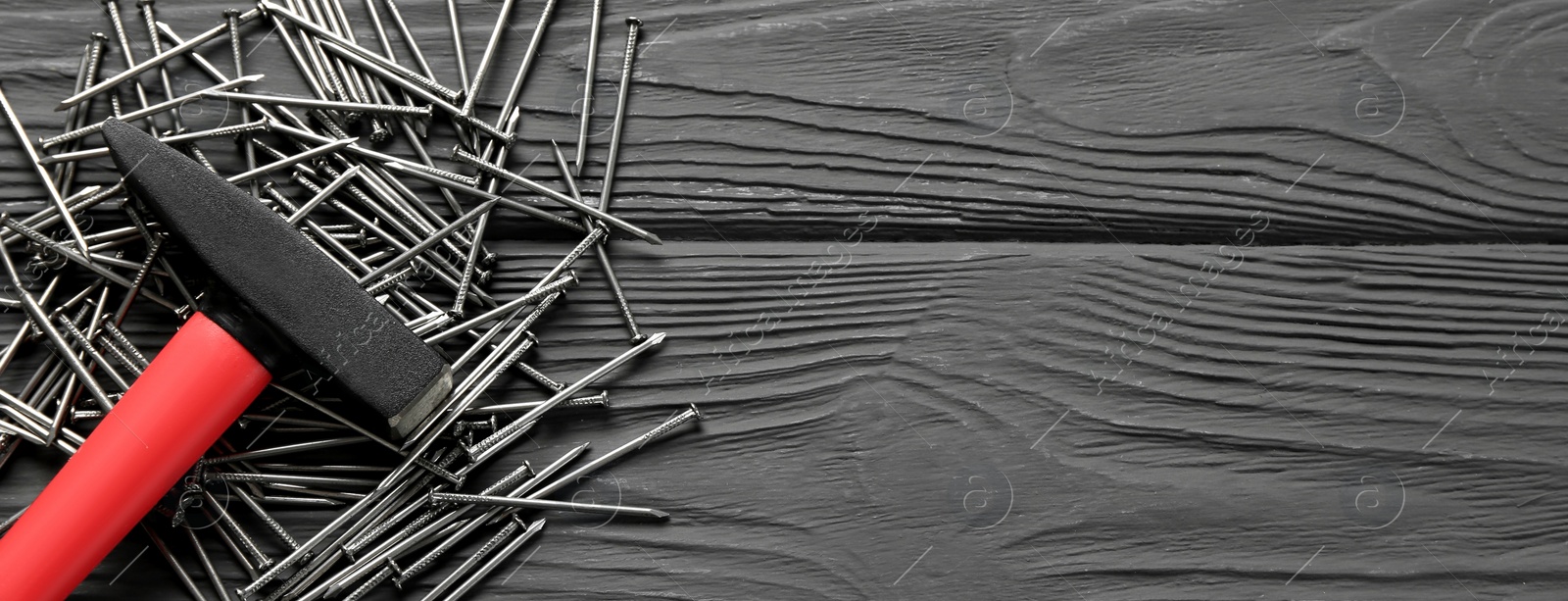 Image of Hammer and metal nails on black wooden table, flat lay with space for text. Banner design