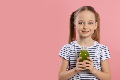 Photo of Cute little girl with bottle of fresh juice on pink background, space for text