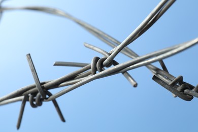 Metal barbed wire on light blue background, closeup