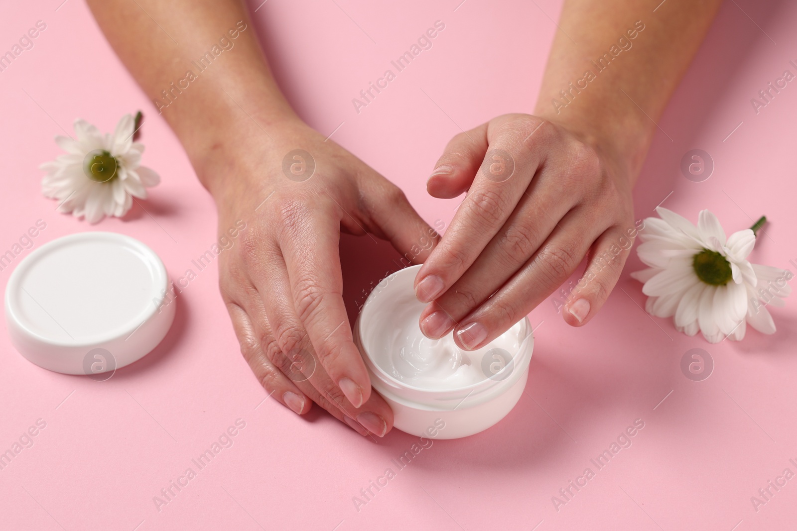 Photo of Woman with jar of hand cream and chamomile flowers on pink background, closeup