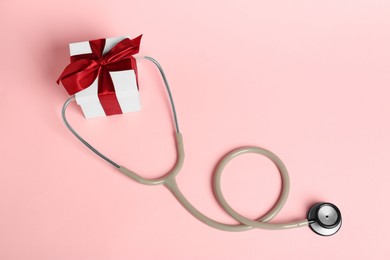 Photo of Stethoscope and gift box on pink background, flat lay. Happy Doctor's Day