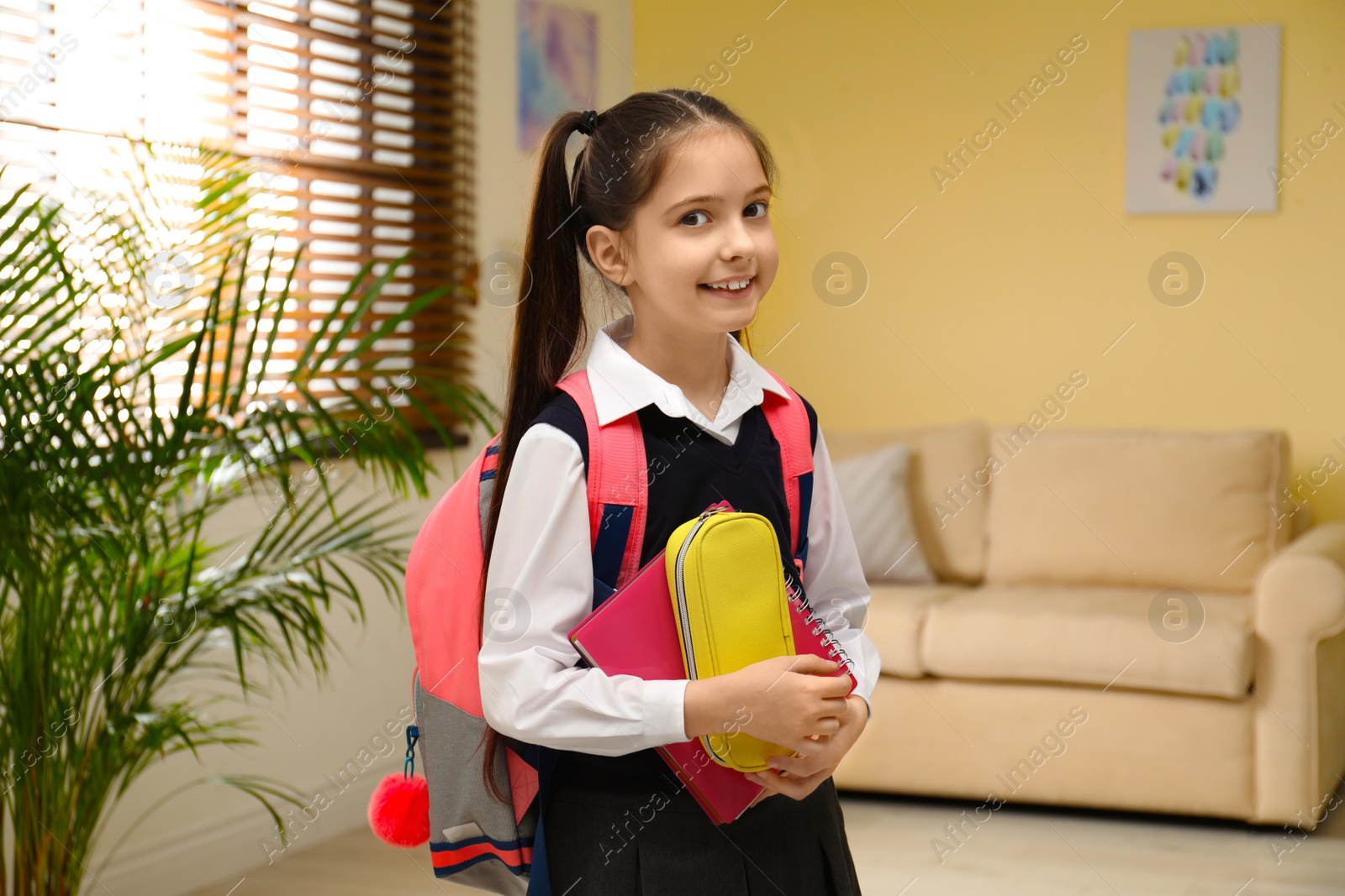 Photo of Little girl in uniform with school stationery at home