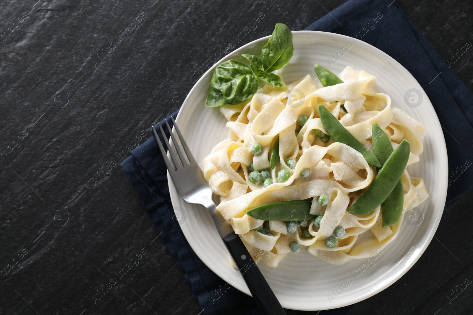 Photo of Delicious pasta with green peas and creamy sauce on black table, top view. Space for text