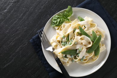 Photo of Delicious pasta with green peas and creamy sauce on black table, top view. Space for text