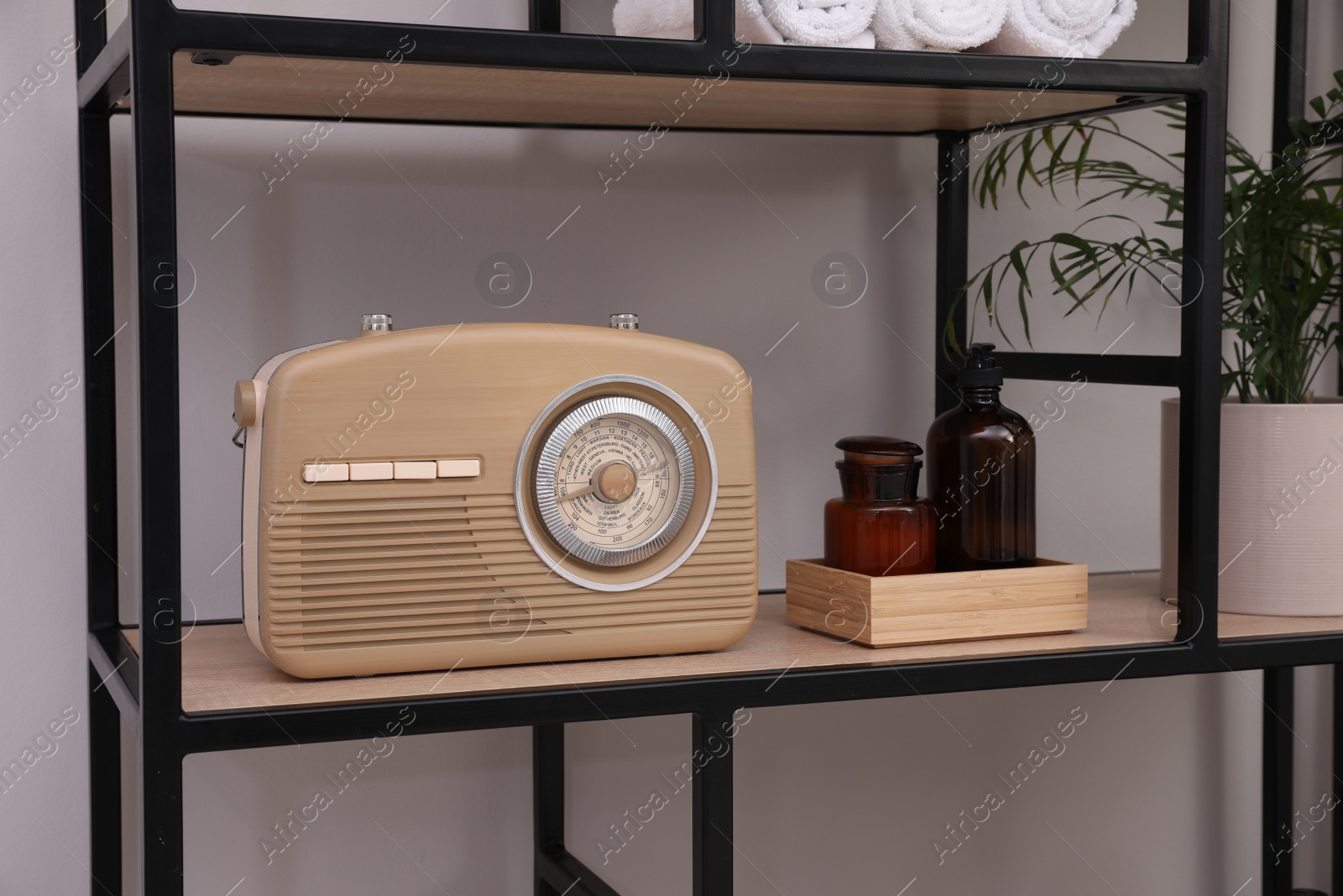 Photo of Stylish beige radio on rack with toiletries and houseplant indoors