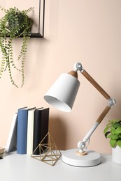 Stylish modern desk lamp, books and plant on table near beige wall indoors