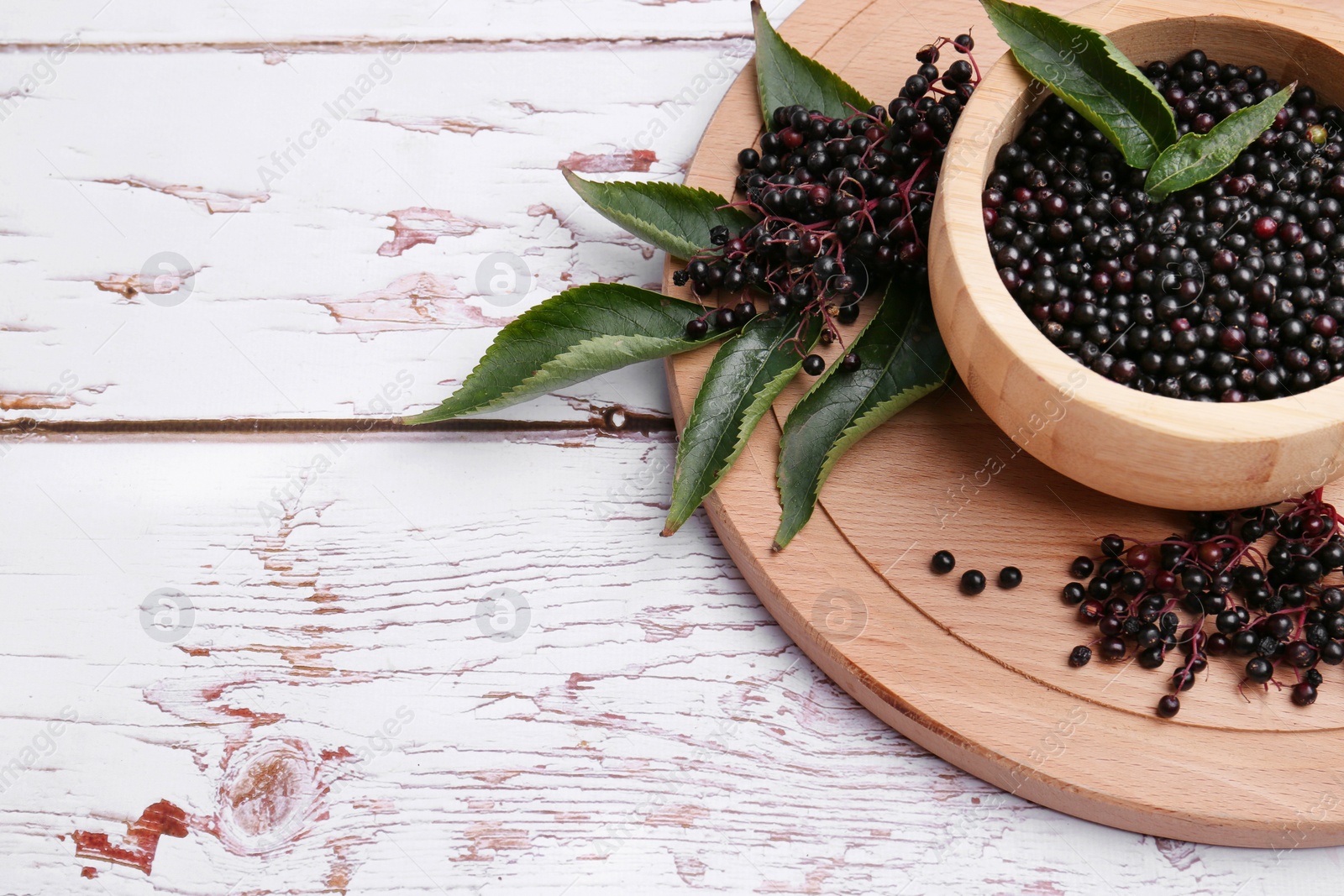 Photo of Tasty elderberries (Sambucus) on white wooden table, space for text