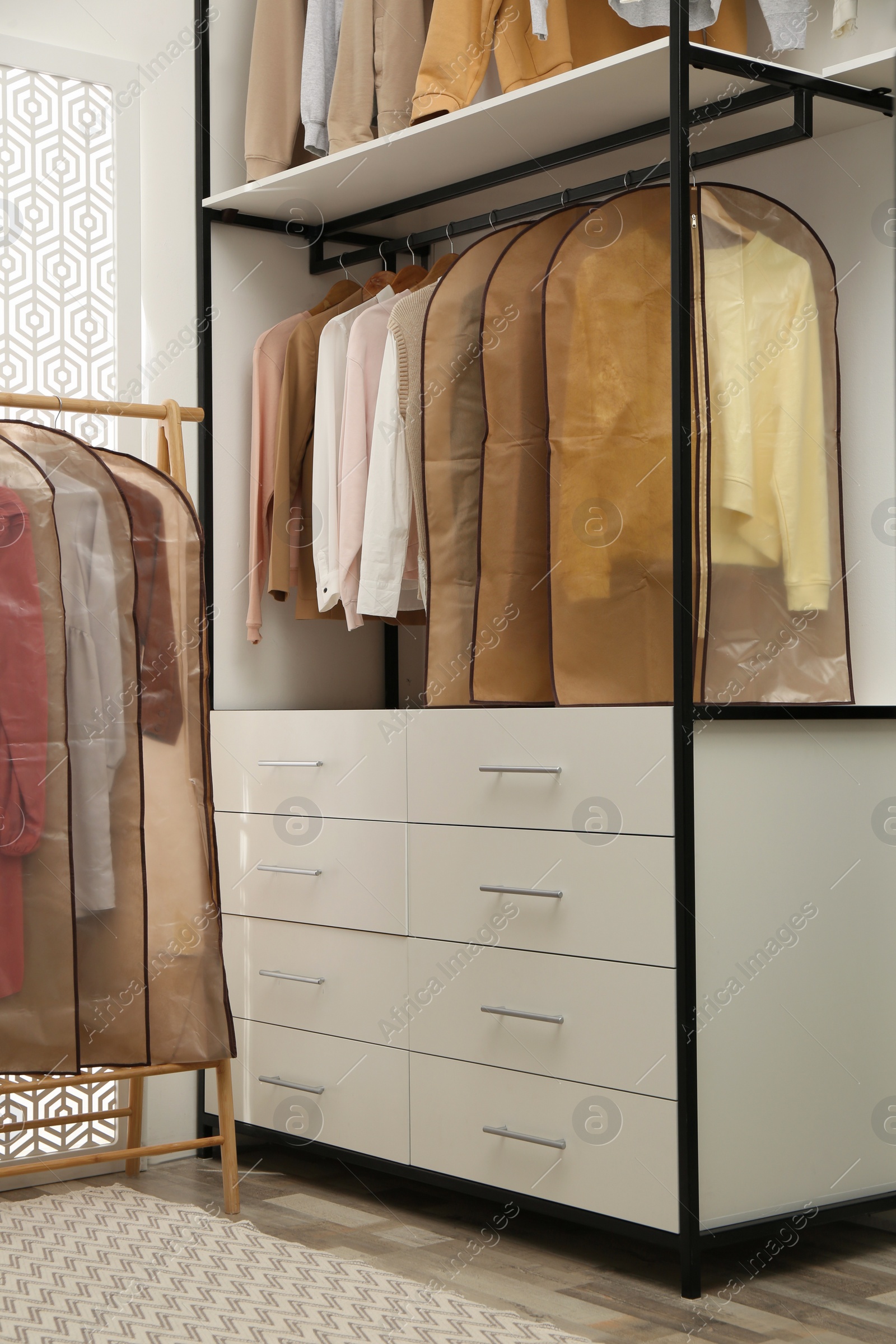 Photo of Garment bags with clothes on rack in dressing room