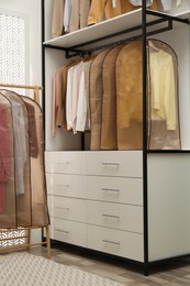 Photo of Garment bags with clothes on rack in dressing room