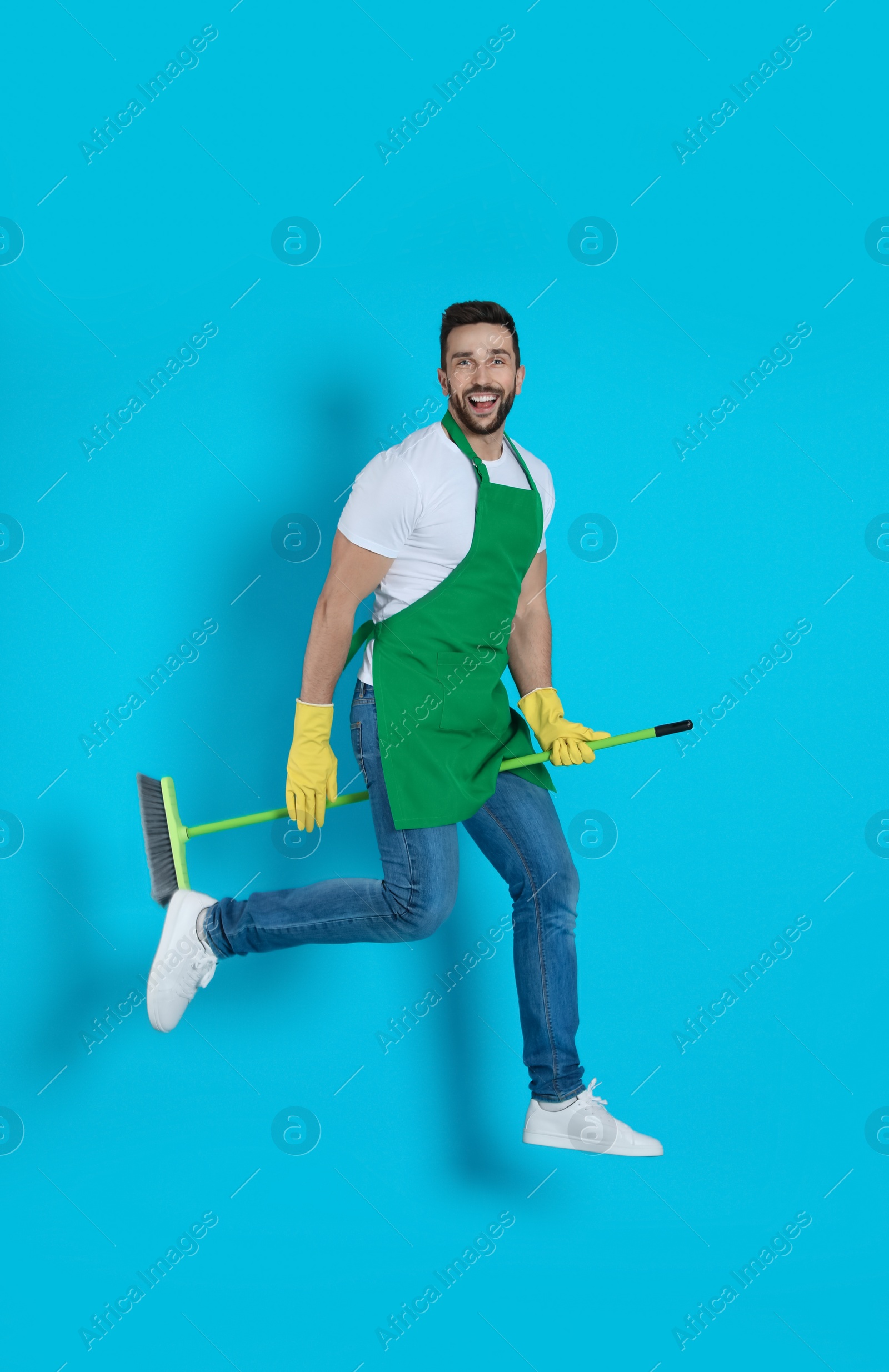 Photo of Man with green broom jumping on light blue background