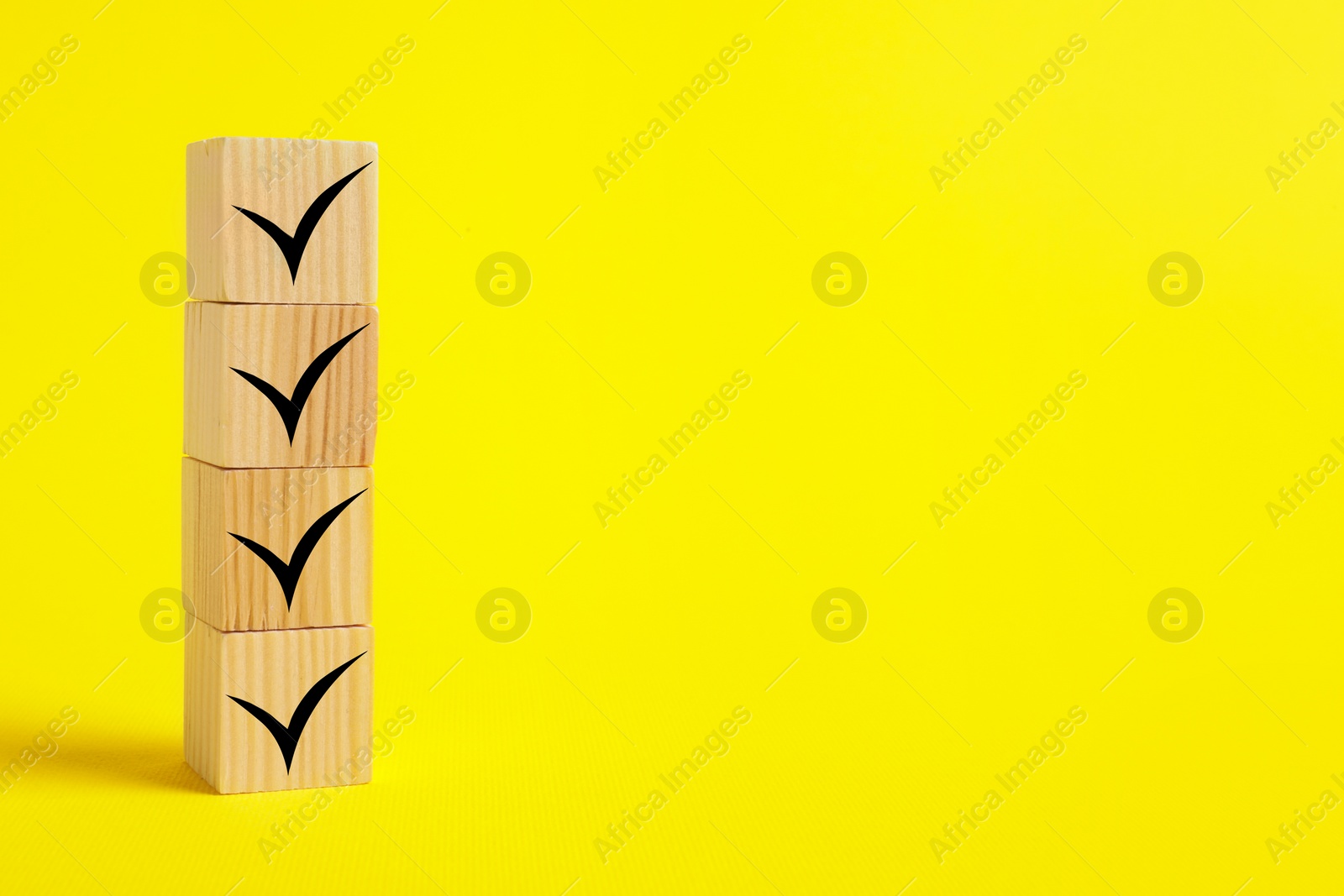 Image of Stacked wooden cubes with check marks on yellow background. Space for text