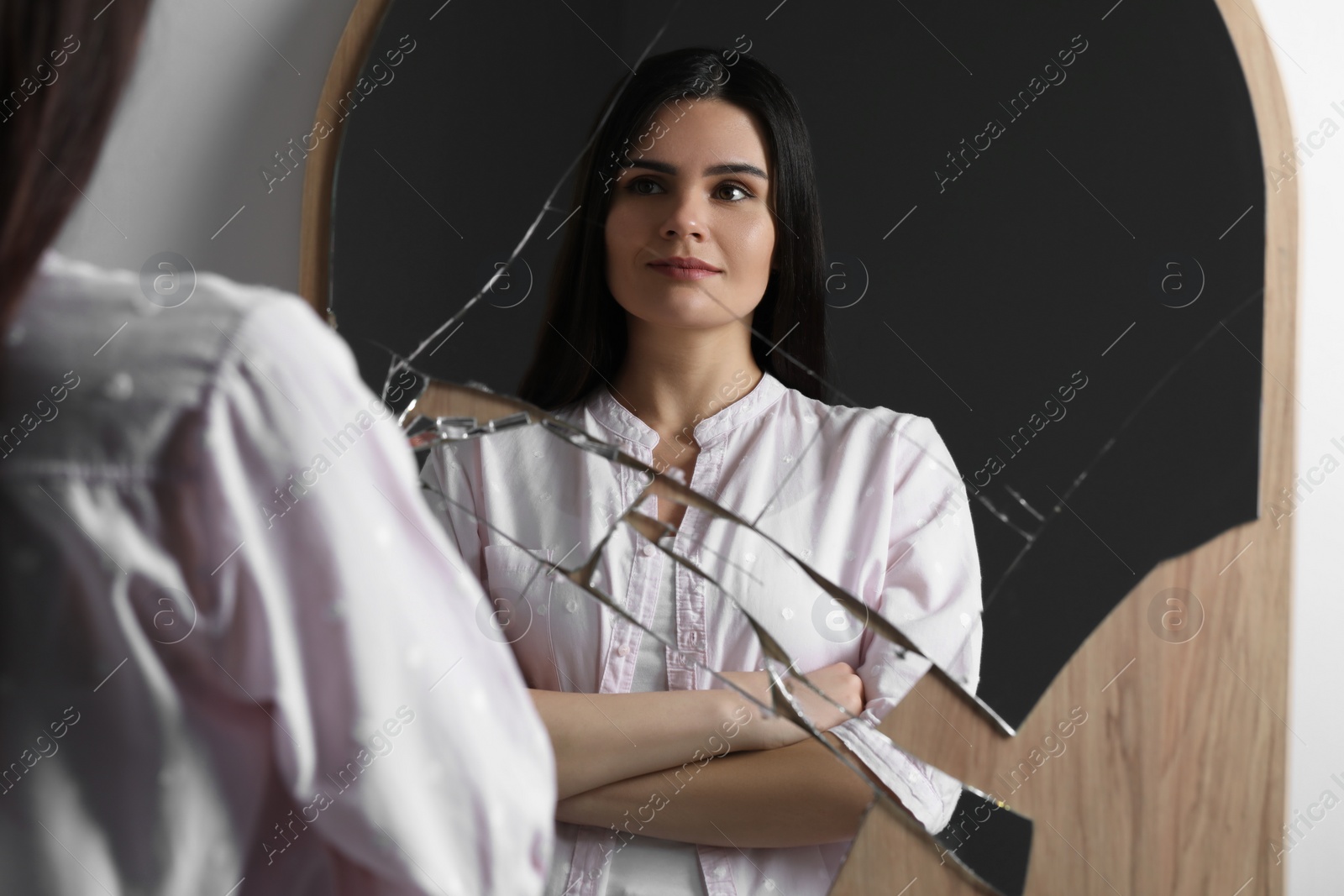 Photo of Young woman looking at herself in broken mirror indoors