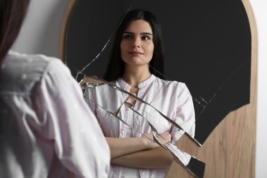 Photo of Young woman looking at herself in broken mirror indoors