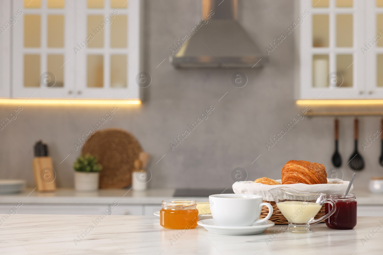 Photo of Breakfast served in kitchen. Fresh croissants, coffee, jam, honey and sweetened condensed milk on white table. Space for text