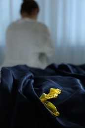 Photo of Woman sitting on bed and unrolled condom in bedroom, selective focus. Safe sex