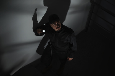 Photo of Male security guard with flashlight on stairs in darkness