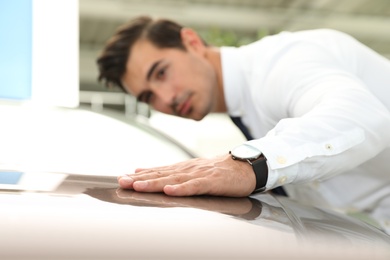 Photo of Young man checking new car in modern dealership, focus on hand