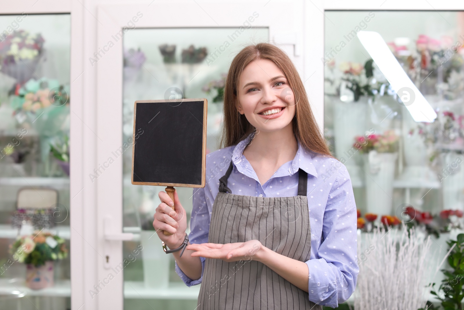 Photo of Female florist holding small chalkboard at workplace