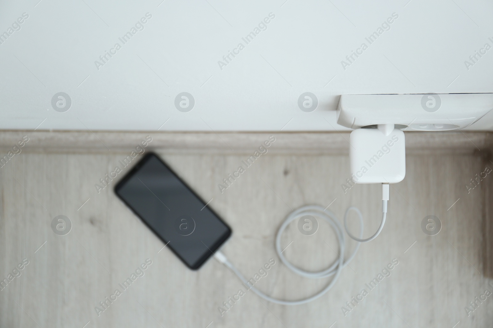 Photo of Modern mobile phone charging from electric socket, top view