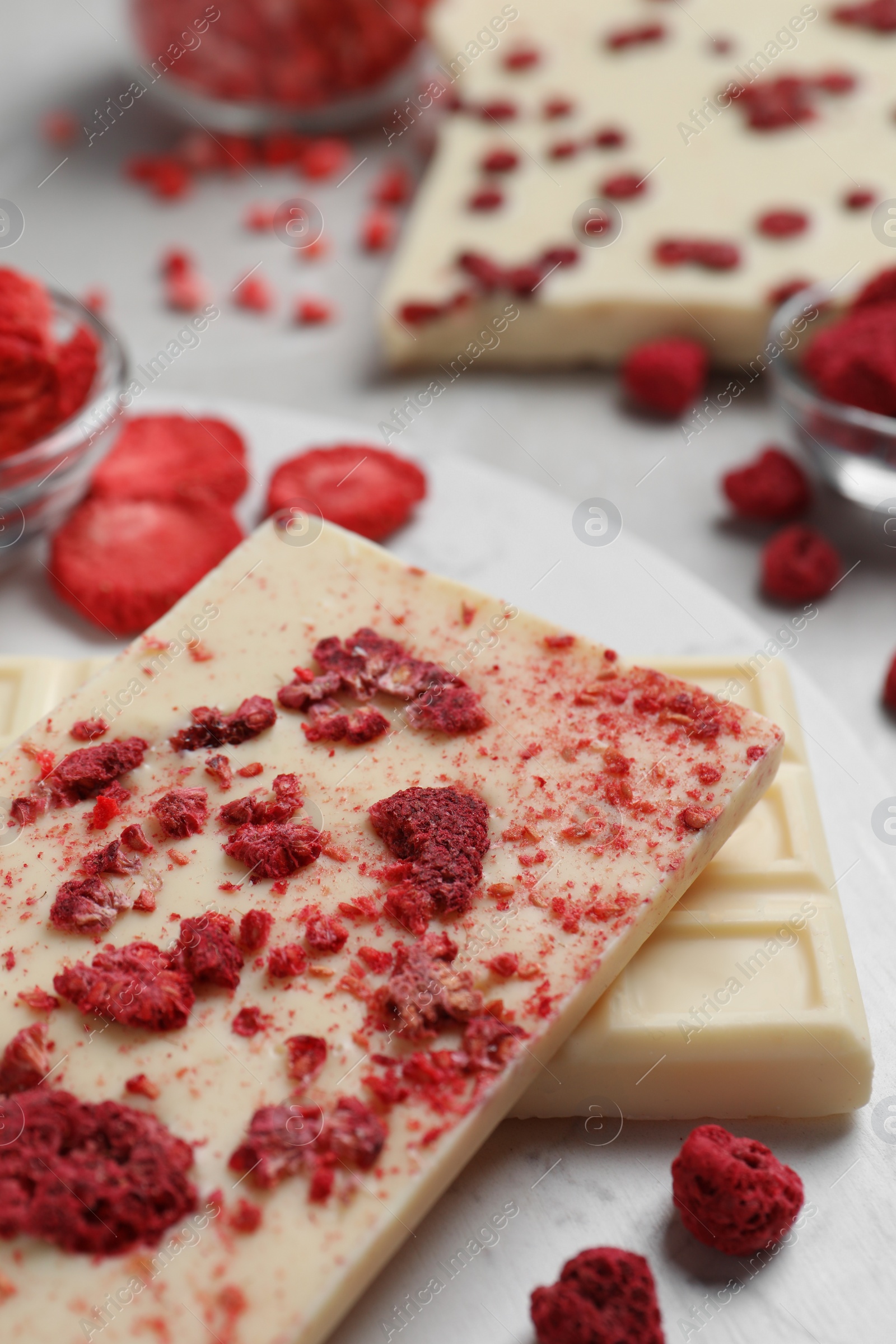 Photo of Chocolate bars with freeze dried raspberries on light marble table, closeup