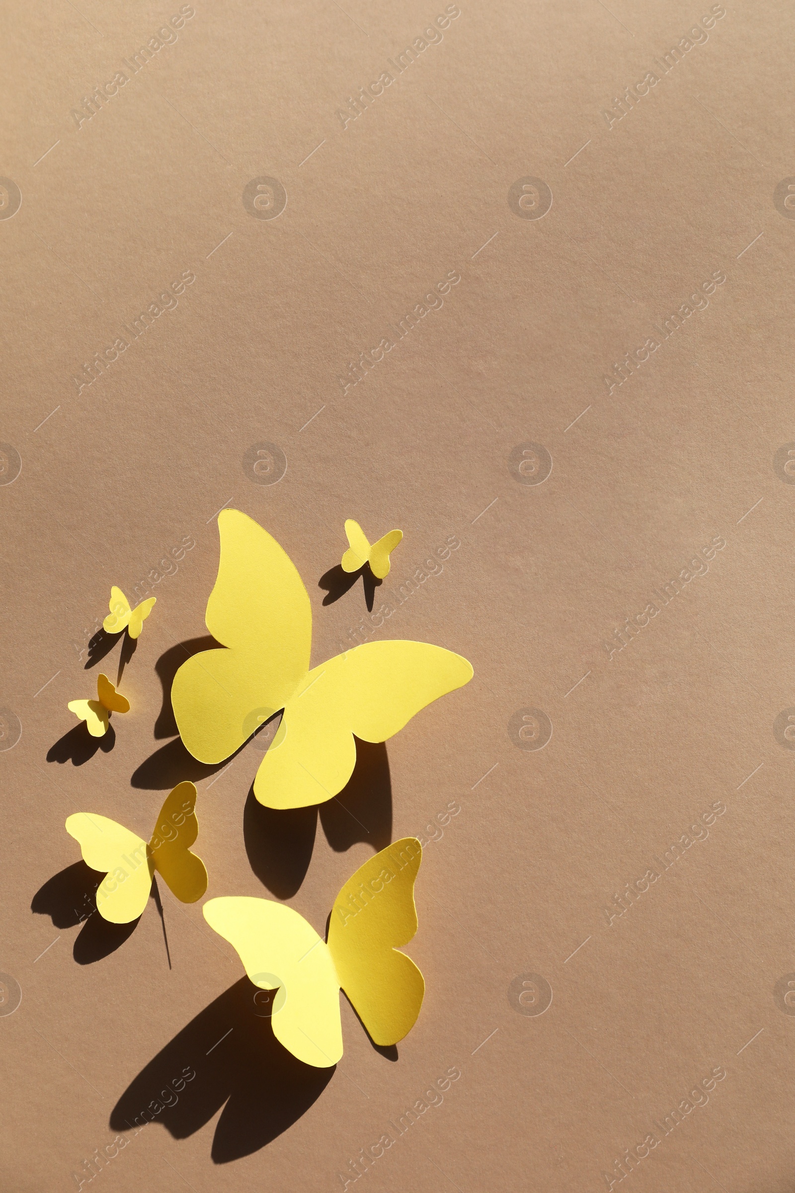 Photo of Yellow paper butterflies on light brown background, top view. Space for text