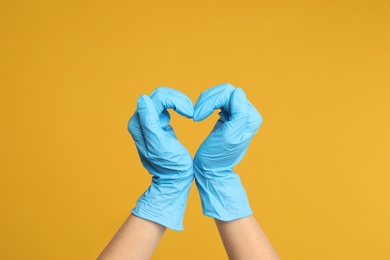 Photo of Doctor in medical gloves showing heart with hands on yellow background, closeup