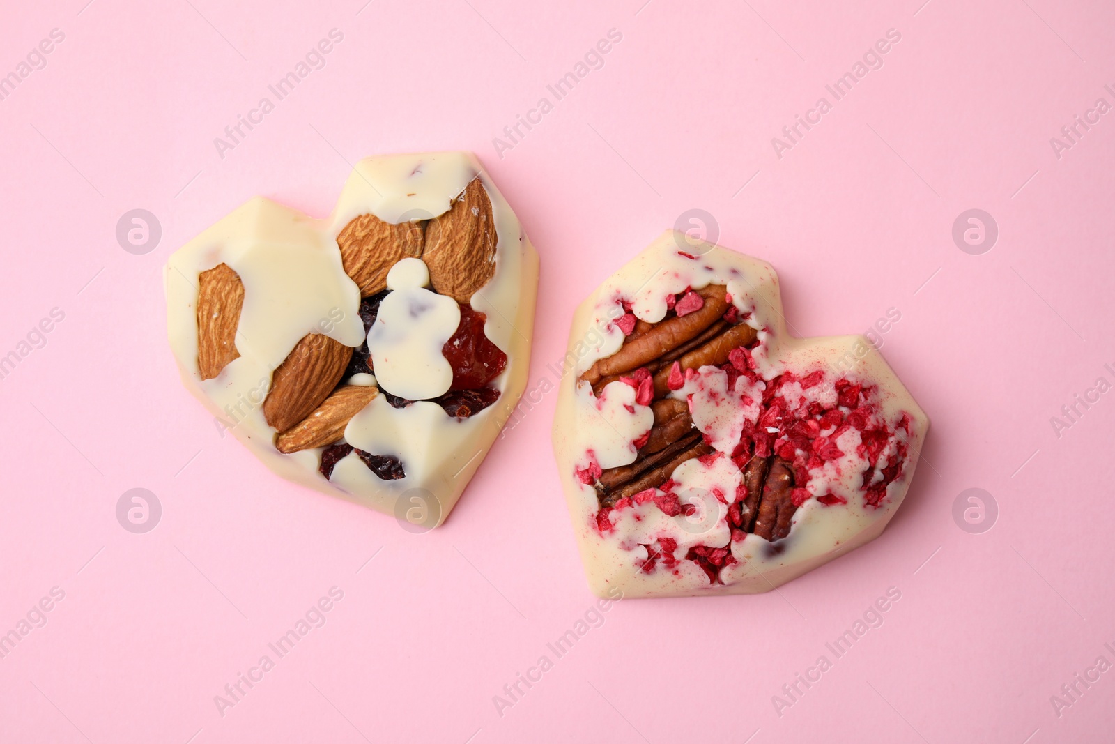 Photo of Tasty chocolate heart shaped candies with nuts on pink background, flat lay