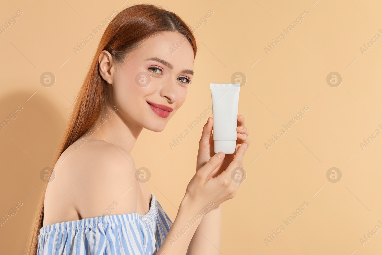 Photo of Beautiful young woman holding sun protection cream on beige background, space for text