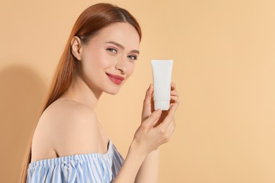 Beautiful young woman holding sun protection cream on beige background, space for text