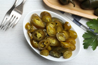 Photo of Bowl with slices of pickled green jalapeno peppers on white wooden table, flat lay