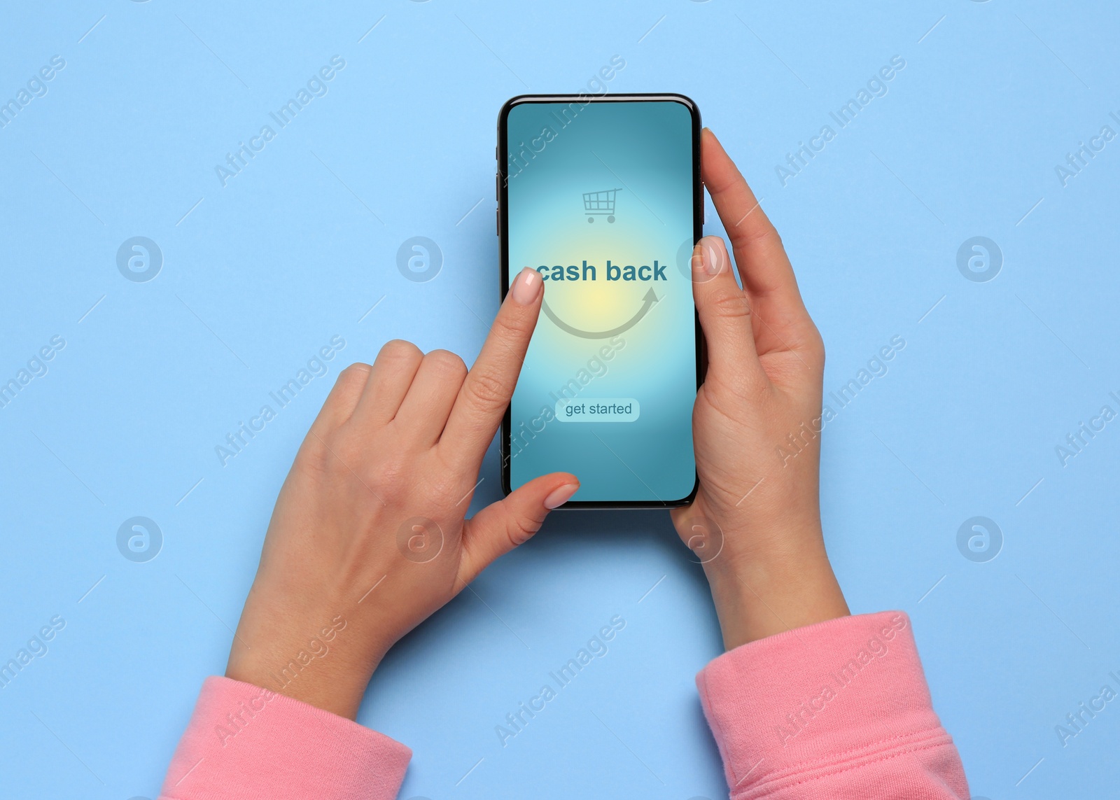 Image of Woman using smartphone with word Cashback and shopping cart icon on light blue background, top view