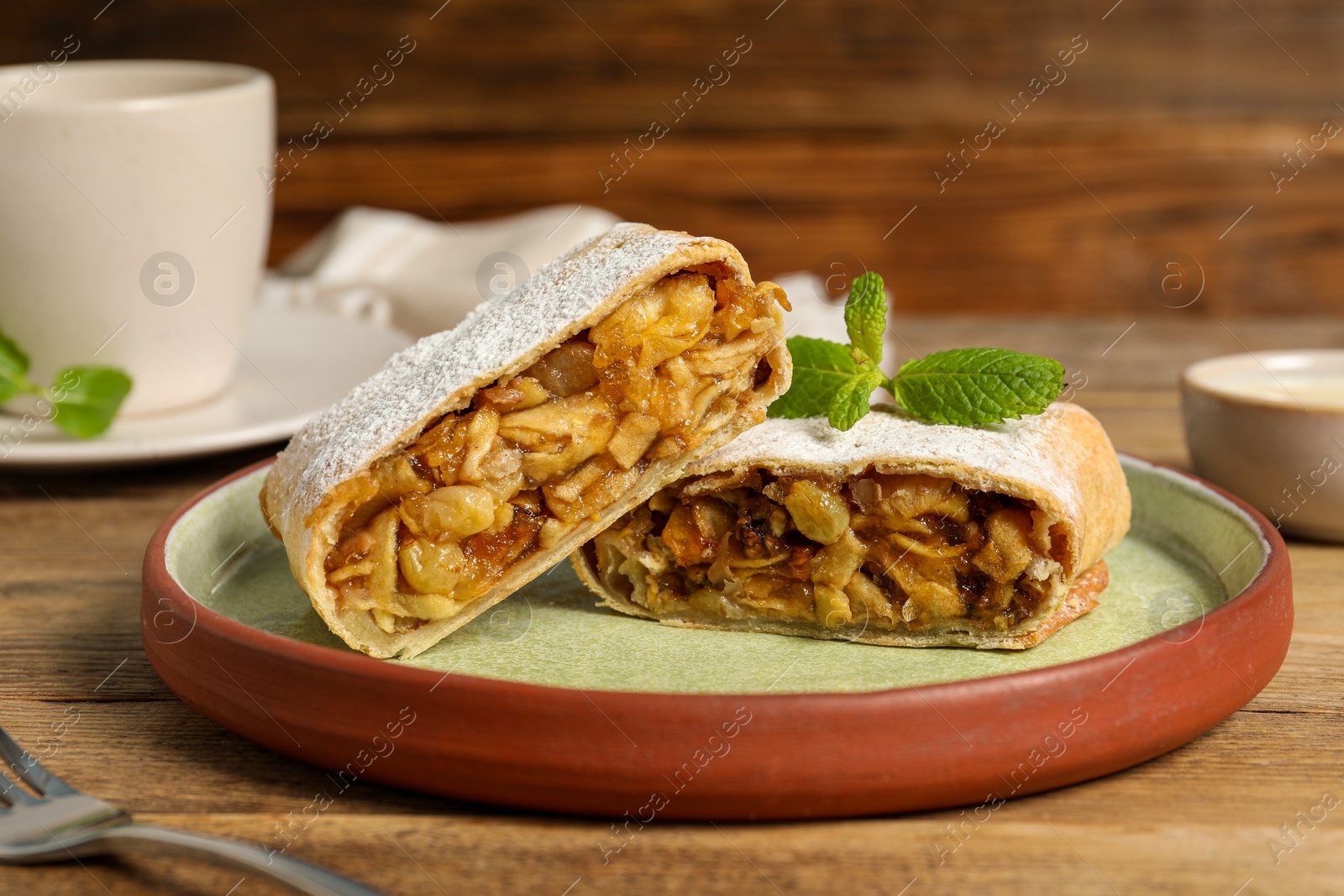 Photo of Delicious strudel with apples, nuts and raisins on wooden table, closeup