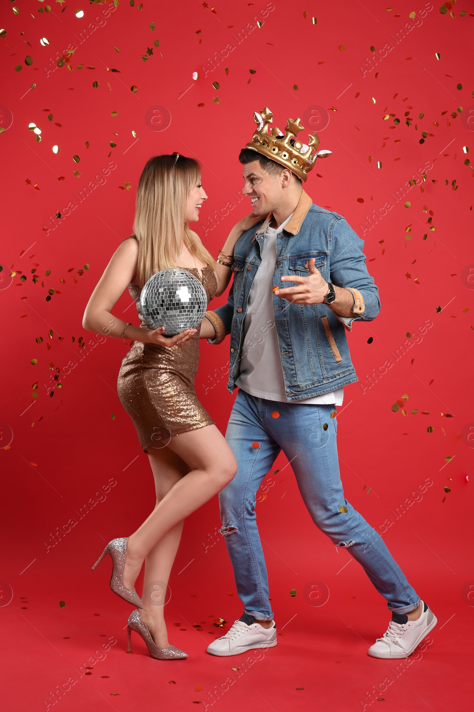 Photo of Happy couple with disco ball and confetti on red background