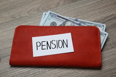 Photo of Card with word Pension, wallet and dollar banknotes on wooden table, closeup