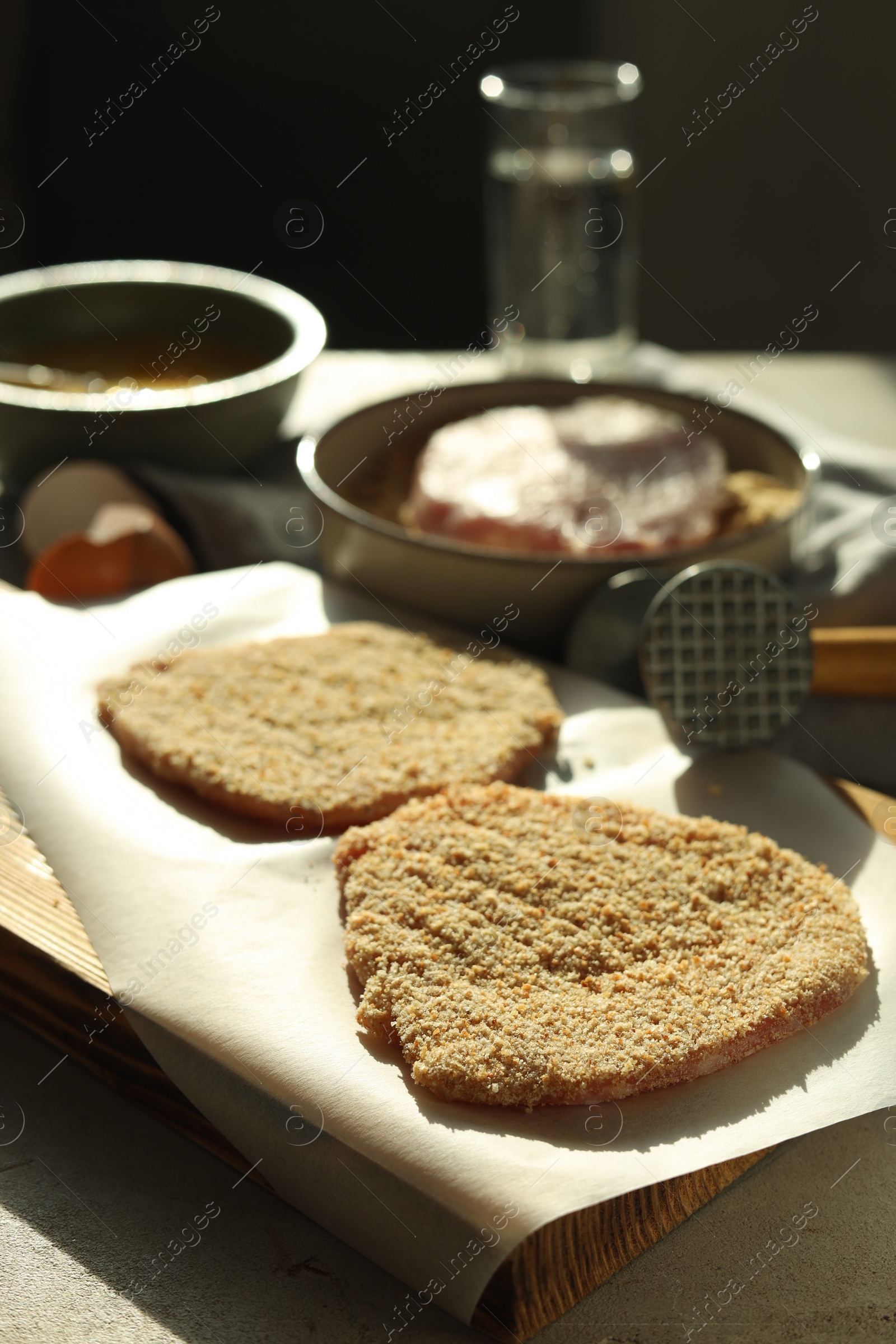 Photo of Cooking schnitzel. Raw pork chops in bread crumbs, meat mallet and ingredients on grey table