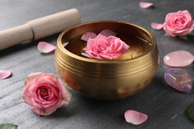 Photo of Tibetan singing bowl with water, beautiful rose flowers, mallet and stones on gray table, closeup