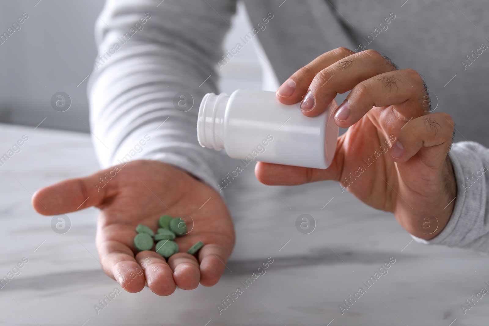 Photo of Man pouring antidepressants from bottle at white marble table, closeup