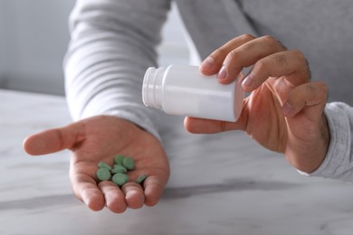 Photo of Man pouring antidepressants from bottle at white marble table, closeup