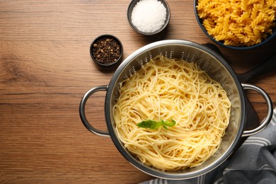 Photo of Cooked pasta in metal colander and spices on wooden table, flat lay. Space for text