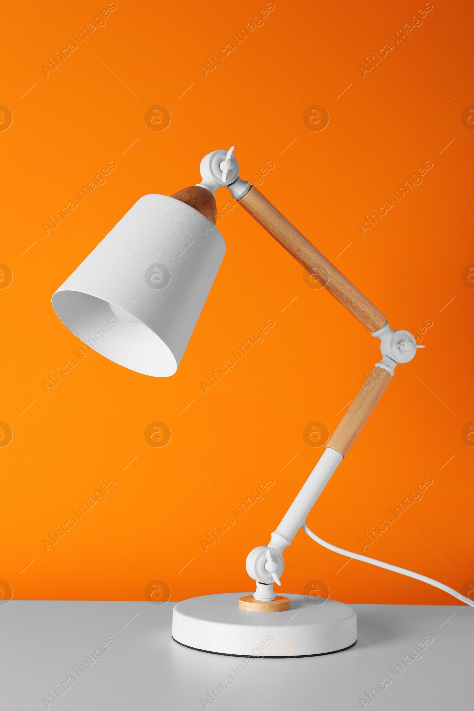 Photo of Stylish modern desk lamp on white table near orange wall