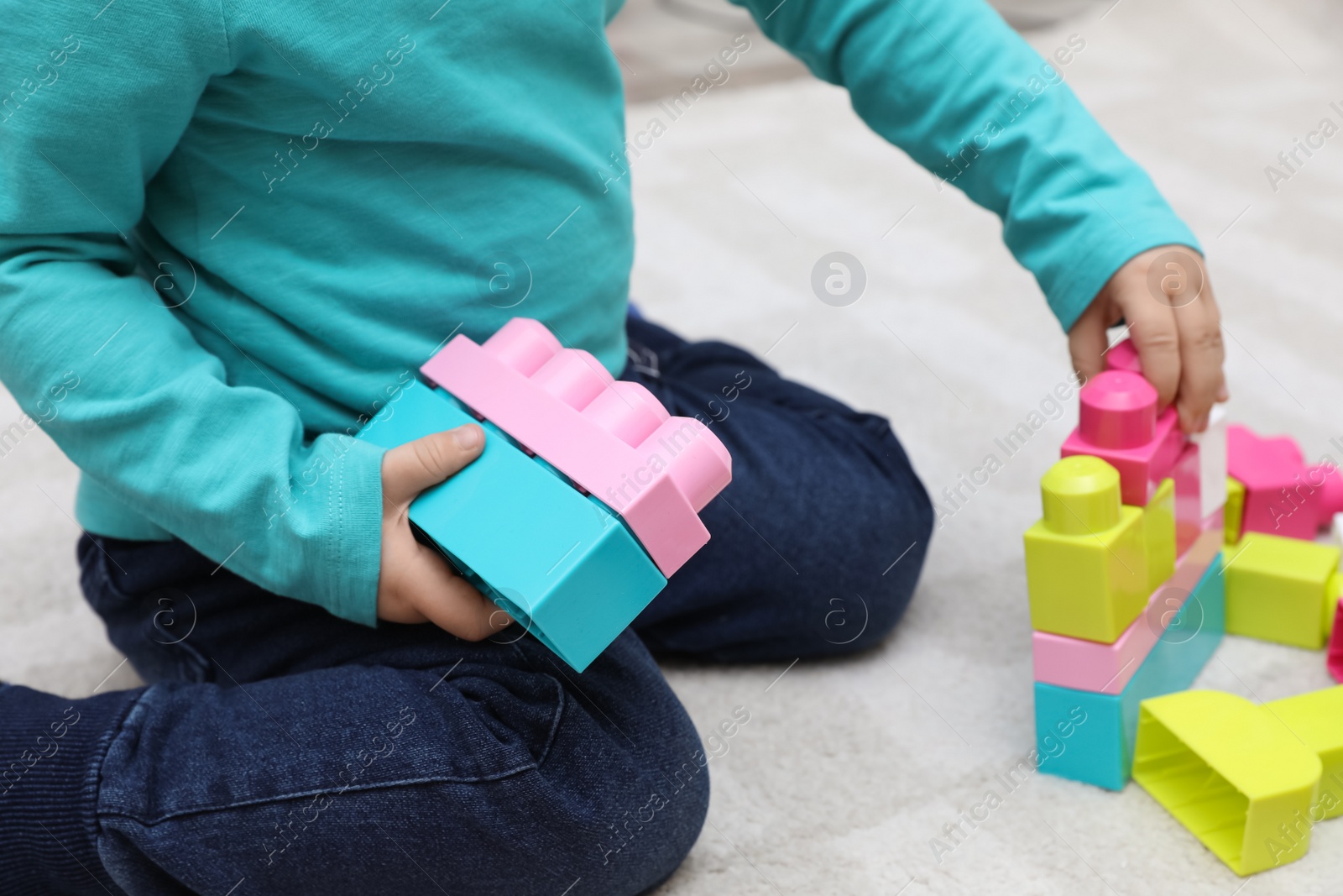 Photo of Little child playing with building blocks on carpet, closeup