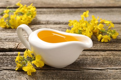 Photo of Rapeseed oil in gravy boat and beautiful yellow flowers on wooden table, closeup